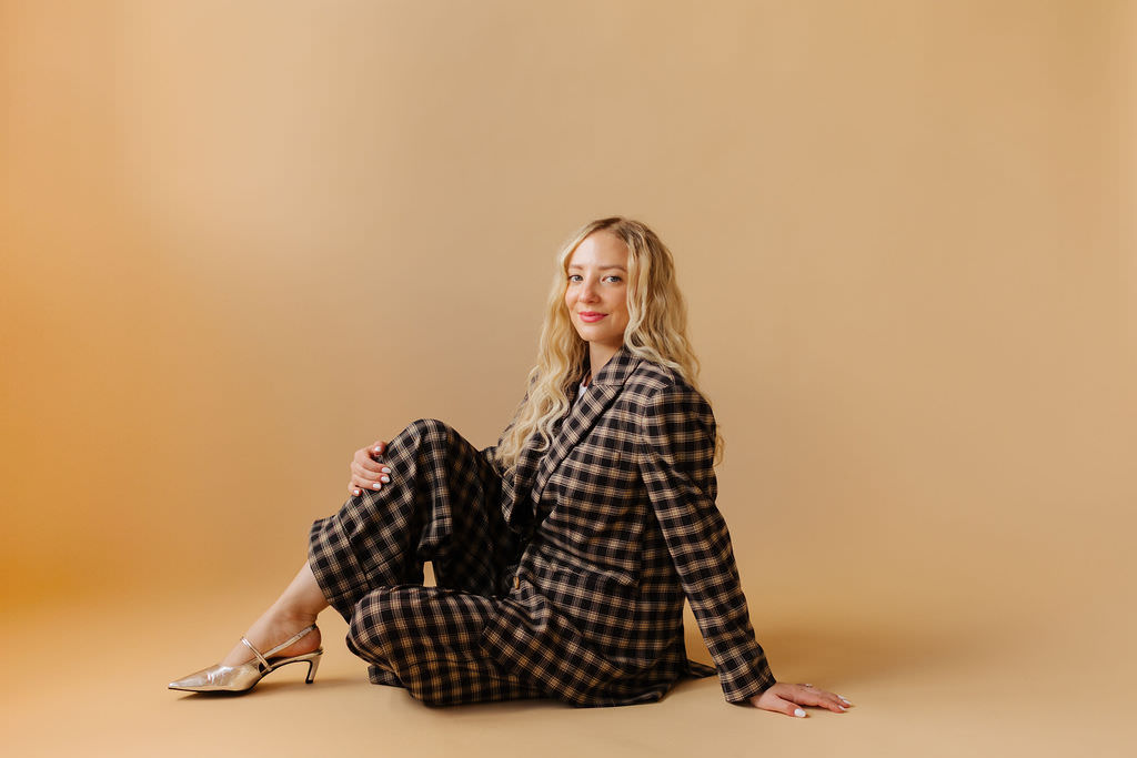 A woman sits in a creative way in a power suit with a smile on her face