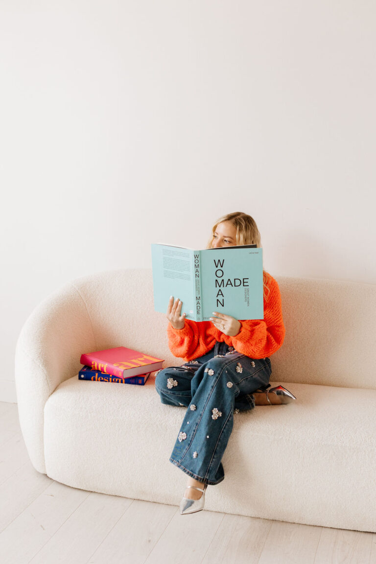 Fashion forward woman on a couch posing with a Woman Made book