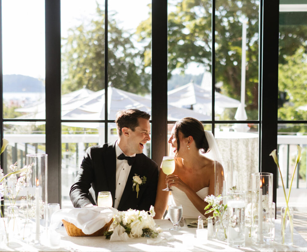 A couple sits at their head table at their reception and laughs with a cheers photographed by a los angeles wedding photographer