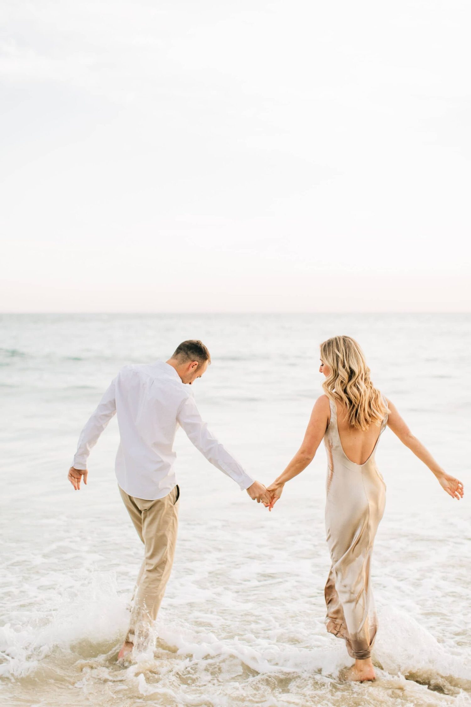 An engagement session with a couple splashing in the ocean in southern california at sunset, photographed by a los angeles wedding photographer