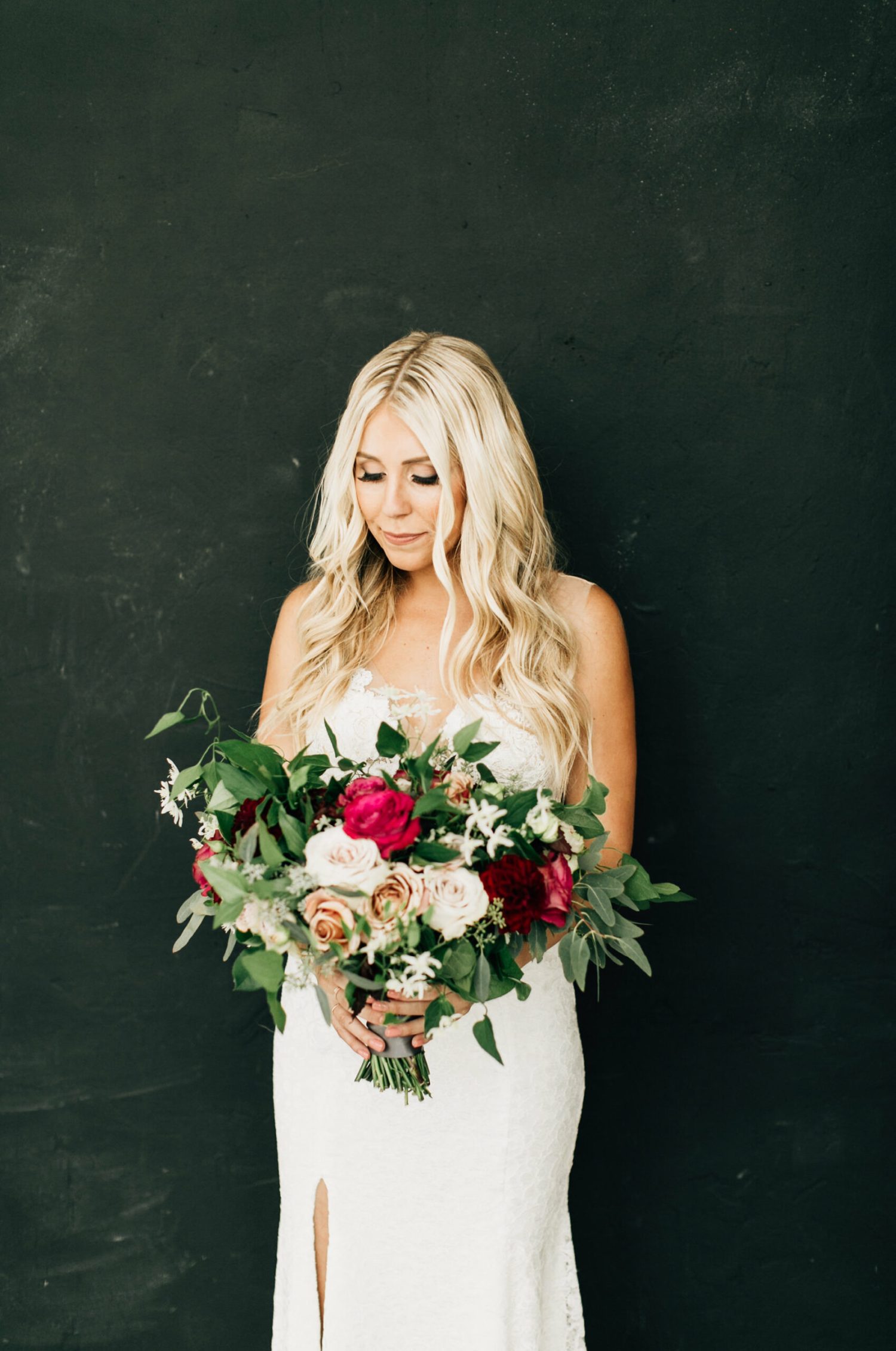A bride against a black wall holding a large floral bouquet shot by a los angeles wedding photogapher